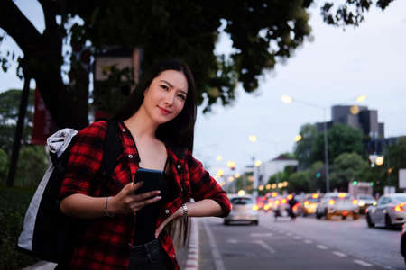Young Asian woman holding smart phone and waiting for taxi on the street.の写真素材