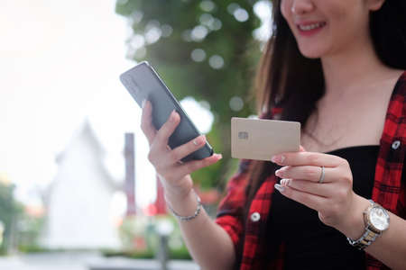 Cropped shot young woman using smart phone and holding credit card for shopping online while sitting at outdoor.の写真素材