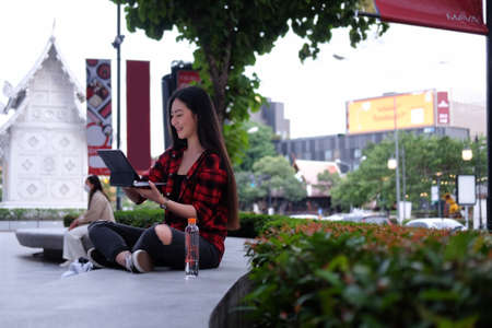 Smiling young woman using laptop computer while sitting in the city park.の写真素材