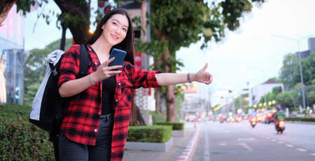 Young smiling Asian woman holding smart phone and calling taxi at city street.の写真素材