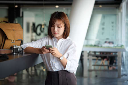 Young Asian woman sitting in modern office and using smart phone.の写真素材