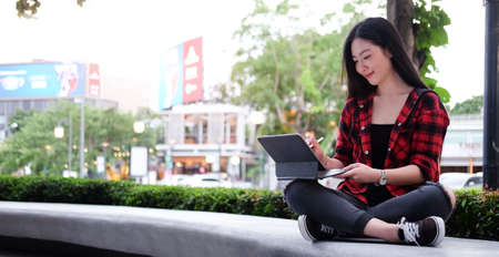 Young Asian woman using laptop computer while sitting outdoors in urban modern city in the evening.の写真素材