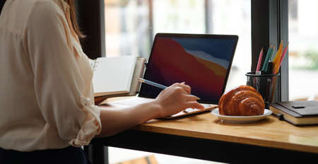 Cropped shot young female holding notebook and working with computer laptop in cafe.の写真素材