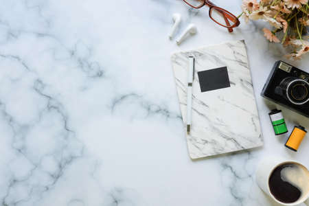 Creative workspace with camera, wireless earphones, coffee cup and notebook on marble table.の写真素材