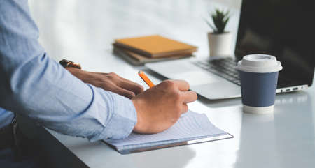 Cropped shot businessman sitting at office desk and making notes on notebook.