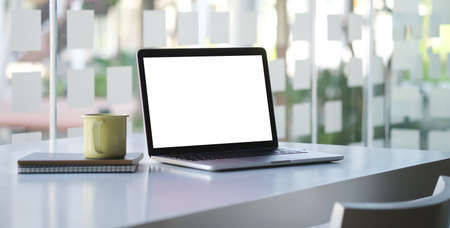 Computer laptop, coffee cup and notebook on white office desk.
