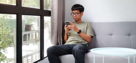 Young Asian man resting on sofa and using smart phone.の写真素材
