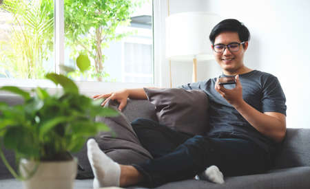 Smiling young man sitting in living room and talking on smart phone.の写真素材
