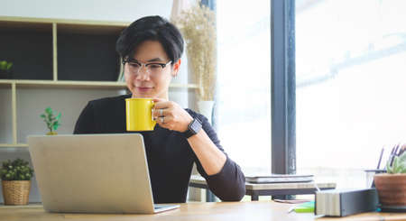 Young asian man drinking coffee and working on laptop computer.の写真素材