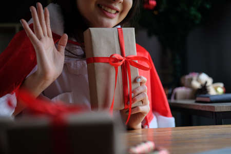 Smiling young woman holding gift box and having video call with family.