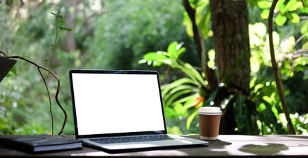 Laptop computer, coffee cup and notebook on wooden table with nature background.の写真素材