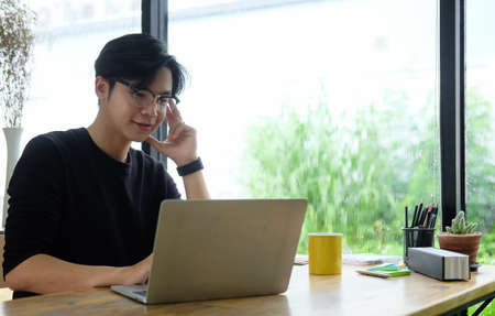Smiling asian man working with laptop computer at home office.