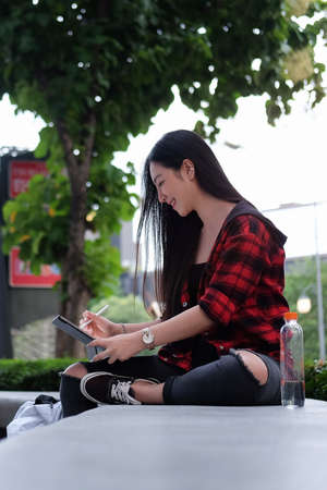 Young Asian woman using laptop computer while sitting outdoors in urban modern city in the evening.の写真素材