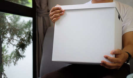Cropped shot young man holding cardboard box with parcel while sitting on sofa at home.