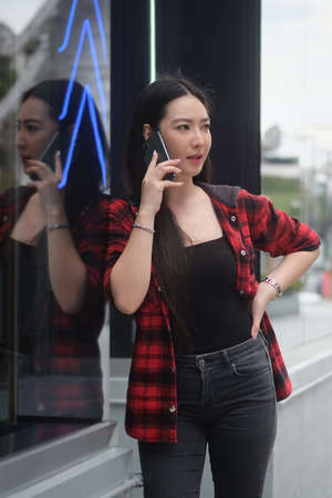 Beautiful young asian woman standing in the city and talking on mobile phone.