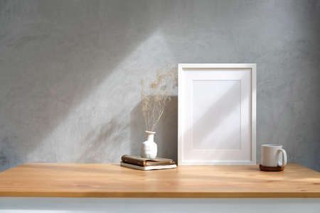 White picture frame, coffee cup, books and vase on wooden table with loft wall. Copy space.