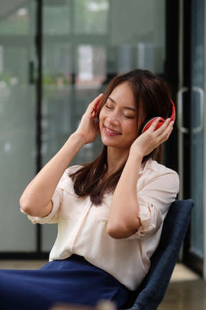 Happy young asian woman closing her eyes and listening to music with wireless headphone.
