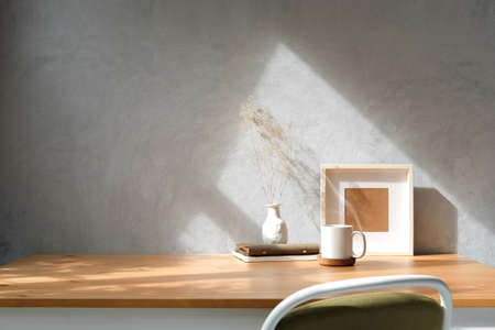 Cup of hot coffee, picture frame and potted plant on wooden table in bright room.