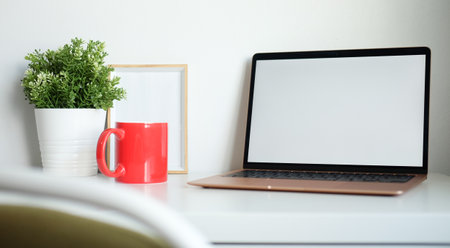 Computer laptop, picture frame, coffee cup and houseplant on white table.の写真素材