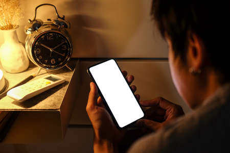 Over shoulder view of young man lying on bed and surfing internet with smart phone.の写真素材
