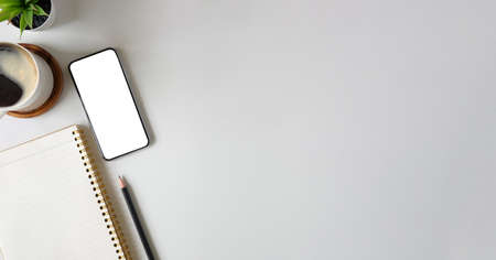 Top view mockup smart phone, notebook, coffee cup and cactus on white table. Blank screen for your...