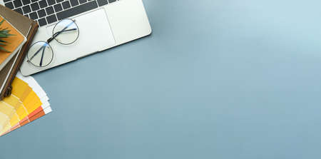 Graphic designer workspace with laptop computer, books, glasses and colour swatch on blue background...