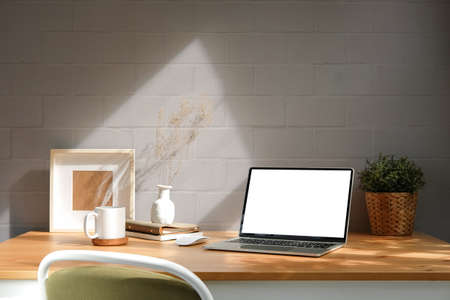 Comfortable workplace, computer laptop, potted plant, coffee cup and picture frame on wooden table.