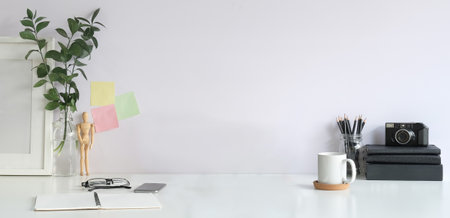 Creative designer workplace with camera, books, coffee cup, picture and houseplant on white table.の写真素材