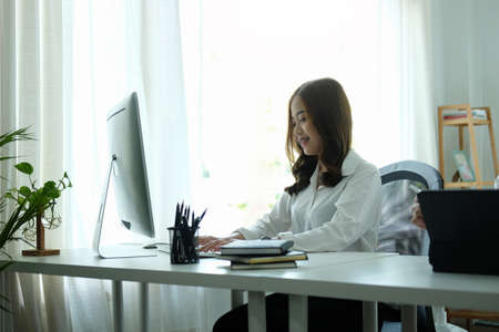 Smiling young asian woman working with computer at modern workplace.