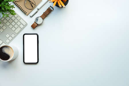 Modern workplace with smart phone, wristwatch, coffee cup and notebook on white table with copy...