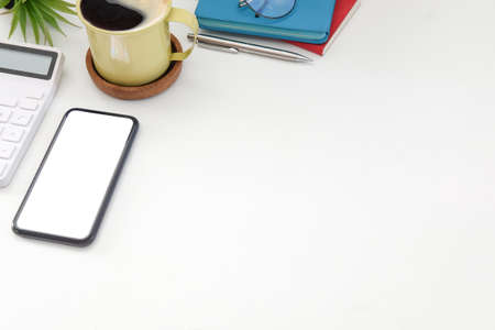 Smart phone, coffee cup, calculator and notebooks on white table.