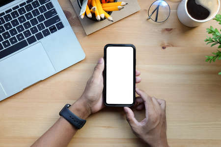 Overhead view man holding mockup smart phone with empty screen on wooden table.の写真素材
