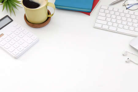 Top view calculator, coffee cup, wireless keyboard and earphones on white office desk.