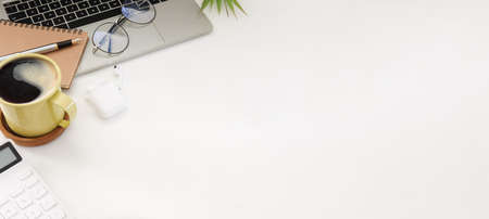 Computer laptop, coffee cup, glasses, calculator and wireless earphone on white office desk.の写真素材