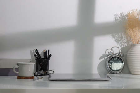 Creative workplace with computer laptop, coffee cup, alarm clock and books on white table.の写真素材