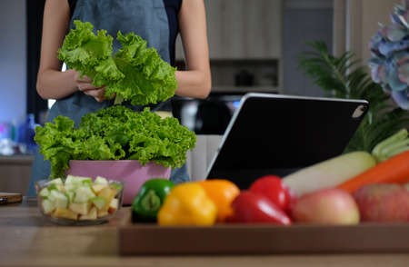Young woman using digital tablet and preparing healthy food in a kitchen. Healthy food and healthy lifestyle concept.の写真素材