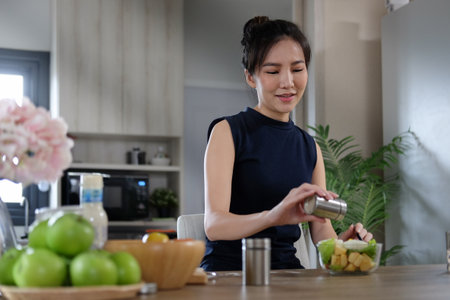 Beautiful asian woman making healthy vegan salad in the kitchen at home.の写真素材
