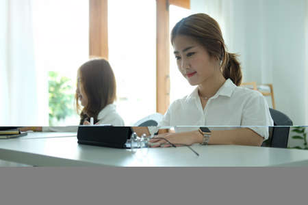 Charming asian woman office worker using computer laptop while sitting with her colleague in office.