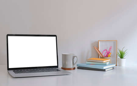 Mockup laptop with empty display, coffee cup, books and picture frame on white table.