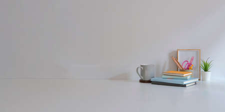 Minimal workplace with books, coffee cup, picture frame and potted plant on white table with copy space.の写真素材