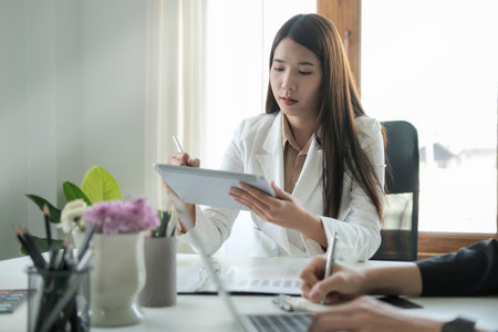 Concentrated young female business leader sitting in conference room and using digital tablet.の写真素材