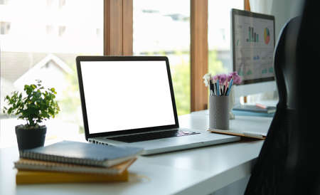 Computer laptop with empty screen, notebook and potted plant on white office desk.の写真素材