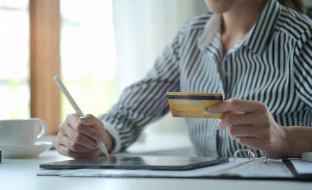Cropped image of young woman holding credit card and using digital tablet.