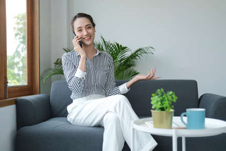 Cheerful businesswoman sitting on couch and talking on mobile phone with her business partner.