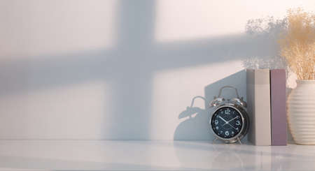 Minimal workplace with books, alarm clock and flower pot on white table.