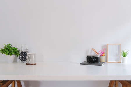 Home office desk with camera, potted plant, coffee cup, stationery and picture frame on white table.の写真素材