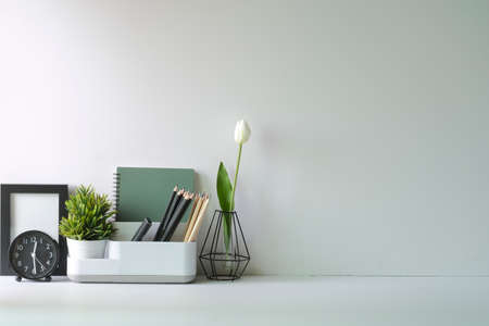 Feminine workplace with picture frame, stationery and flower pot on white table. Copy space.の写真素材