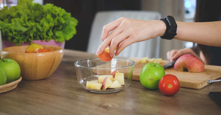 Woman cutting apple on wooden board, preparing fruit salad in the kitchen.