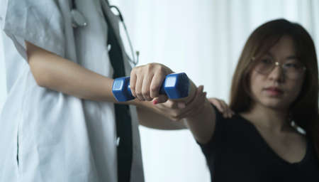 Therapist assisting patient exercises dumbbell in rehabilitation clinic. Concept of physio treatment.の写真素材