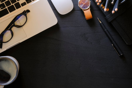 Computer laptop, glasses, coffee cup on black wooden background. Top view.